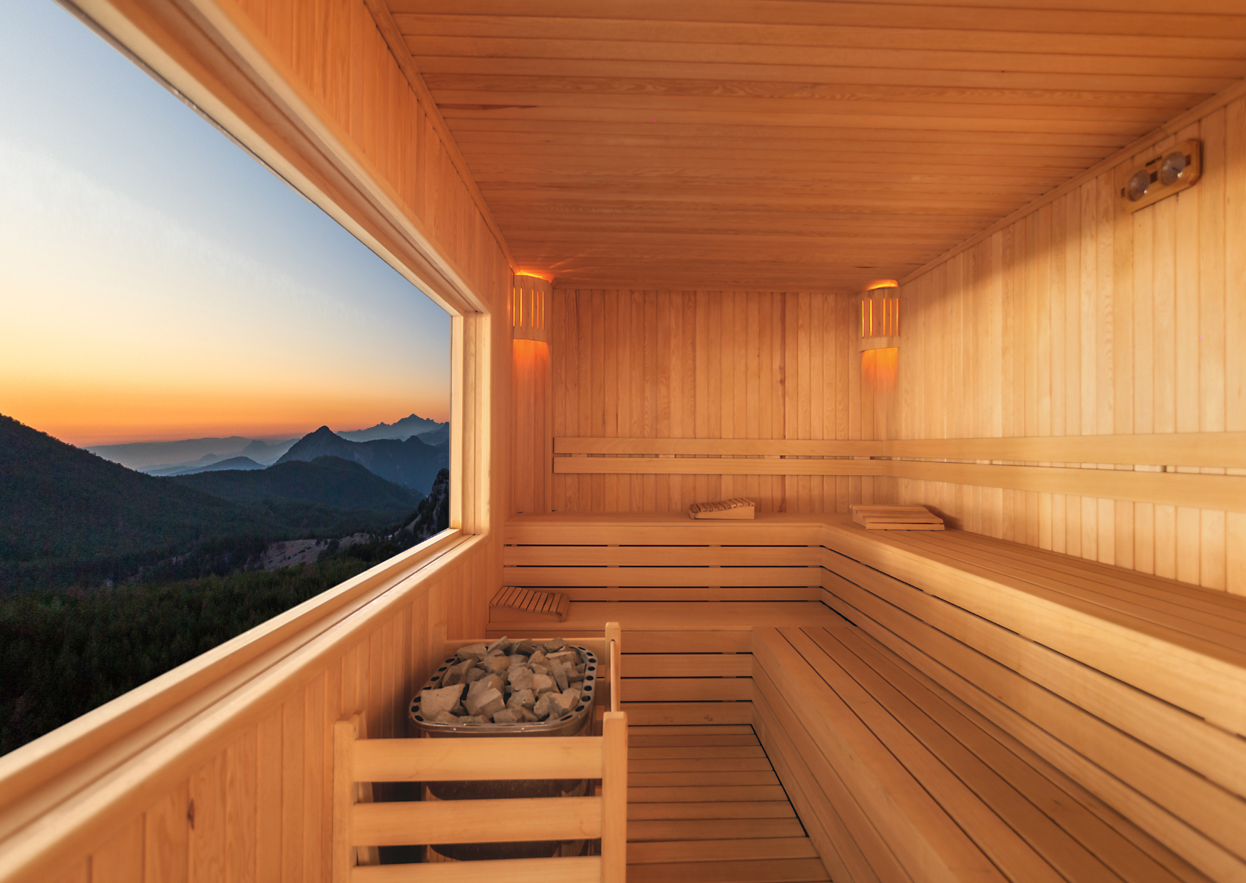 Innenraum eines Saunafasses aus Holz mit Panoramafenster und Blick auf Berge bei Sonnenuntergang
