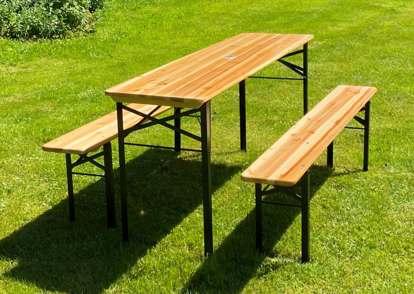 Klappbare Bierzeltgarnitur aus hellem Holz mit Tisch und zwei Bänken auf einer grünen Wiese